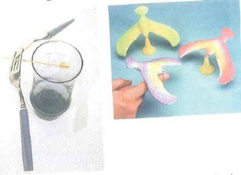 Explain the balancing acts in Fig. Where are the centers of gravity FIGURE Balancing acts Left: A toothpick on the rim of the glass supports a fork and spoon. Right: Toy birds balance on their beaks. See Conceptual Question.