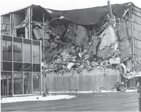 <strong>Consider the below photograph. What does this illustrate about the nature of earthquake destruction?</strong> A) Earthquake destruction takes a long time to occur. In a year's time, the seemingly intact building may look the same as the destroyed building. B) Earthquake destruction is <u> not </u> widespread. It often destroys only a building or two. C) Different building codes matter greatly. Buildings that can take earthquake stresses often survive without damage while others build differently face total destruction. D) Earthquake destruction is very sporadic. Like tornadoes, it may hit one street block hard and completely miss another.