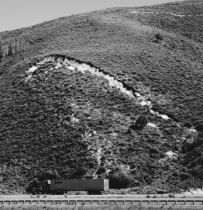 <strong>In the figure below,what would be the most effective way to stabilize the slope,assuming that the slope is in a dry,desert environment? </strong> A)regrade the slope B)move the road C)add more vegetation D)install riprap