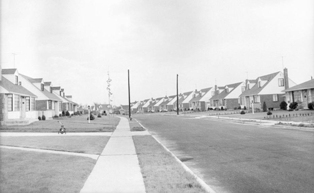 <strong> Based on this photograph of this street scene in Levittown, New York, what was one distinguishing feature of the postwar suburbs?</strong> A) standardized homes lacking any distinguishing characteristics B) narrow streets that made driving cars difficult C) lack of yards for gardening or for children to play in D) lack of safe paths for children to get to school or for walkers