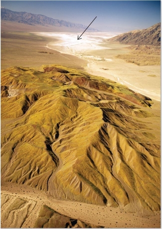 <strong> What desert feature is visible in this image, indicated by an arrow?</strong> A)Playa lake B)Desert varnish C)Sand dunes D)Inselberg