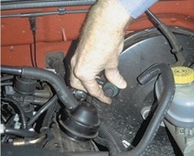 <strong>What component is the technician holding in this photograph? </strong> A)Fluid plug B)Check valve C)Vacuum sensor D)Vacuum elbow